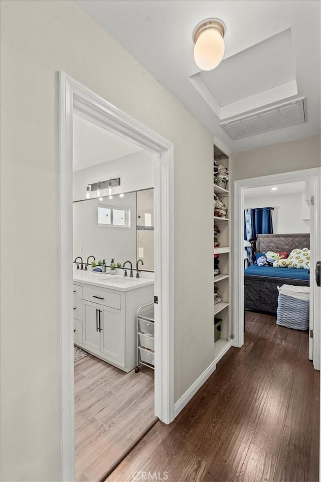 corridor featuring a sink, wood finished floors, visible vents, and baseboards