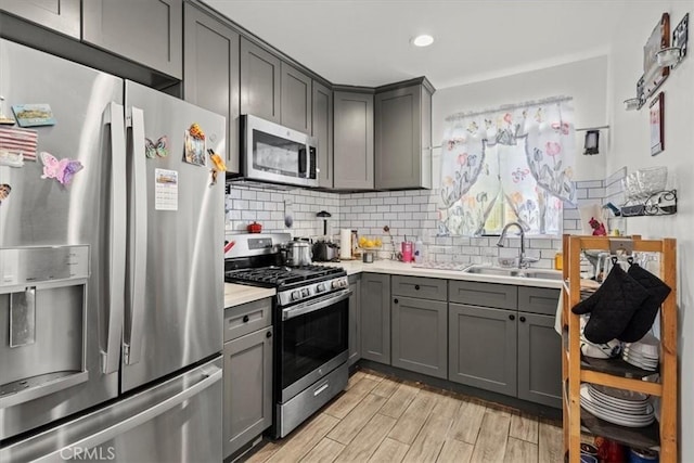 kitchen featuring tasteful backsplash, gray cabinets, stainless steel appliances, and a sink