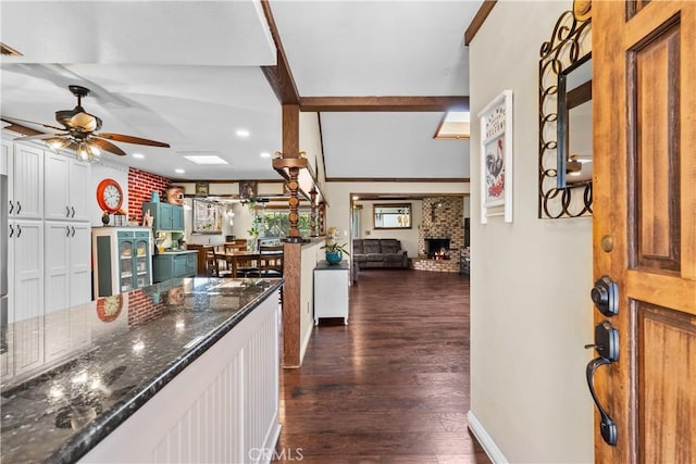 kitchen featuring a brick fireplace, ceiling fan, wine cooler, dark stone counters, and beam ceiling