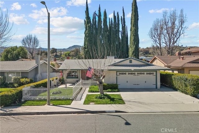 ranch-style home featuring stucco siding, concrete driveway, a garage, a fenced front yard, and a mountain view