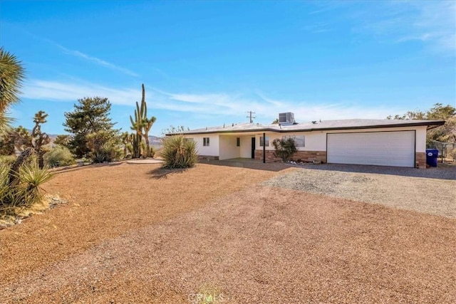 ranch-style house featuring cooling unit, stone siding, a garage, and gravel driveway