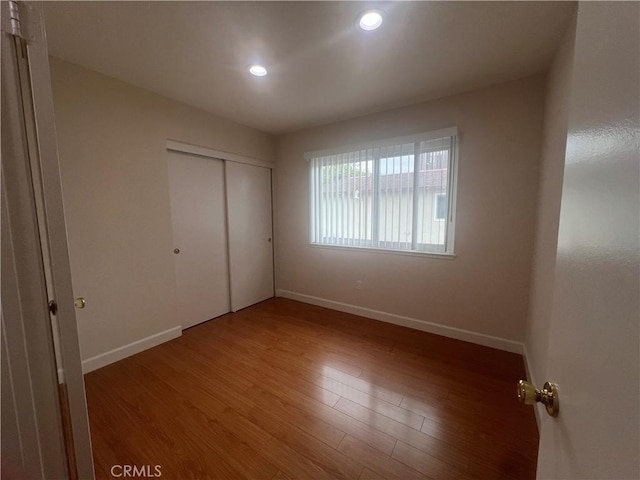 unfurnished bedroom featuring a closet, baseboards, wood finished floors, and recessed lighting