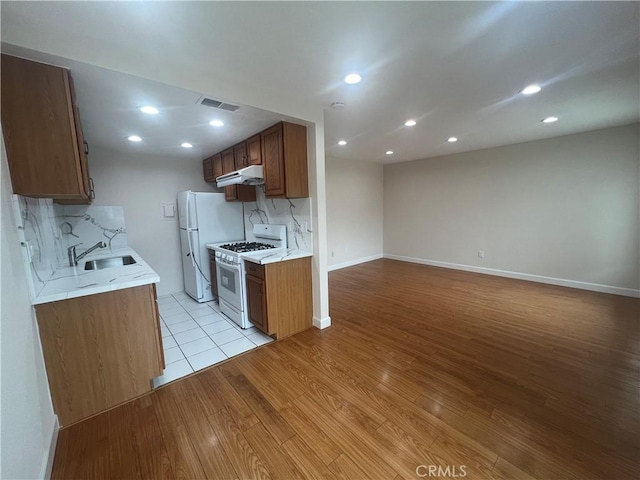 kitchen with under cabinet range hood, white appliances, light countertops, light wood-type flooring, and backsplash