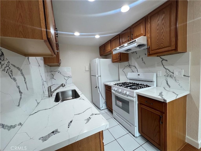kitchen with white appliances, decorative backsplash, brown cabinets, under cabinet range hood, and a sink