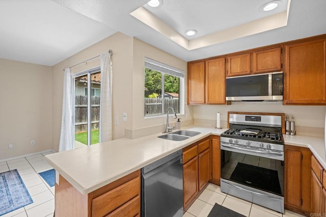 kitchen featuring a raised ceiling, light countertops, appliances with stainless steel finishes, brown cabinetry, and a sink