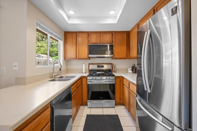 kitchen with light tile patterned floors, a raised ceiling, appliances with stainless steel finishes, brown cabinetry, and a sink