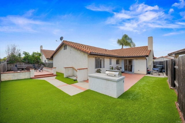 back of property featuring a fenced backyard, a chimney, an outdoor kitchen, and a tile roof