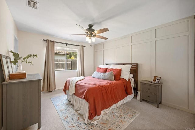 bedroom with light carpet, ceiling fan, visible vents, and a decorative wall