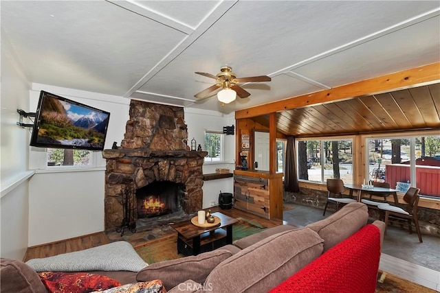 living room featuring a wealth of natural light, beam ceiling, ceiling fan, and a stone fireplace