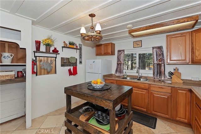 kitchen with brown cabinetry, freestanding refrigerator, hanging light fixtures, a sink, and beam ceiling