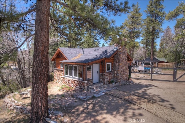 view of front of home with stone siding, roof with shingles, fence, and driveway