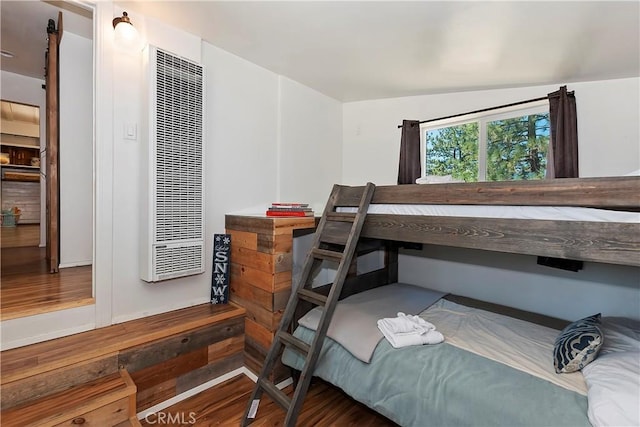 bedroom with a heating unit and wood finished floors