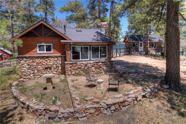 rear view of house featuring stone siding, roof with shingles, and fence