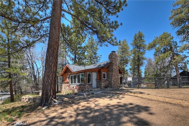 view of front facade with stone siding, a chimney, and fence