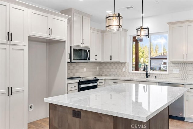 kitchen with a kitchen island, a sink, stainless steel appliances, light wood-type flooring, and backsplash