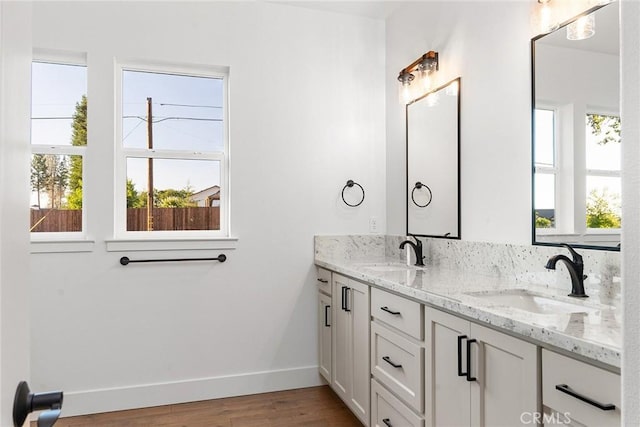 full bath with double vanity, baseboards, a sink, and wood finished floors