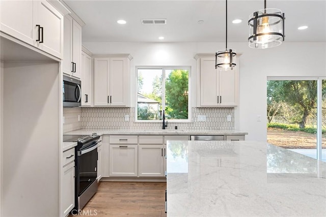 kitchen with light wood finished floors, tasteful backsplash, visible vents, stainless steel appliances, and a sink