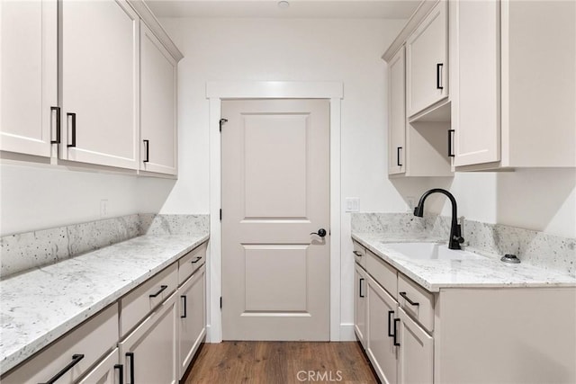 kitchen featuring wood finished floors, a sink, light stone counters, and white cabinets