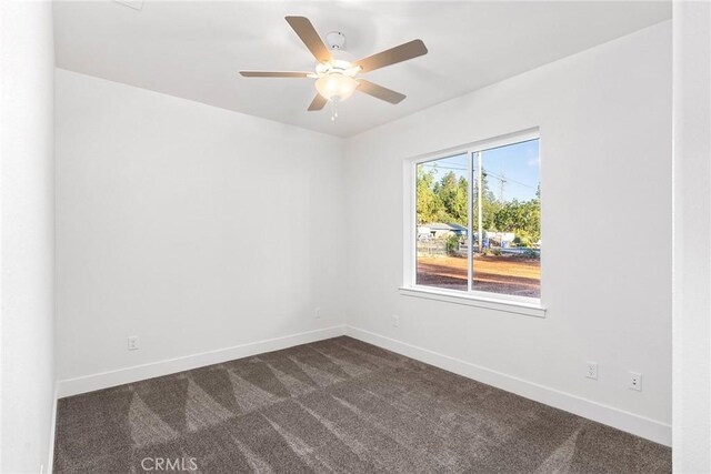 empty room with dark colored carpet, a ceiling fan, and baseboards