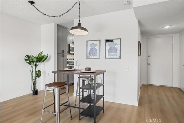 dining space featuring baseboards, light wood-type flooring, and a textured ceiling