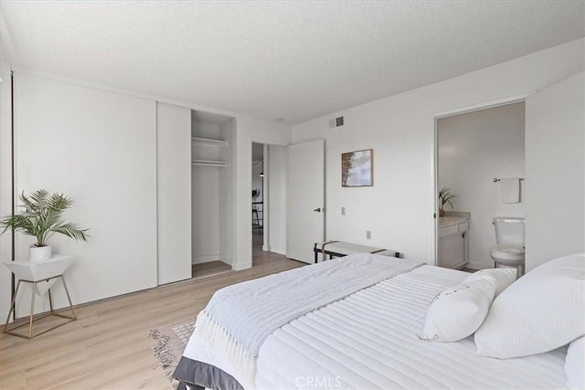 bedroom with visible vents, wood finished floors, a closet, a textured ceiling, and ensuite bath