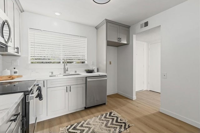 kitchen featuring visible vents, gray cabinetry, a sink, light wood-style floors, and appliances with stainless steel finishes