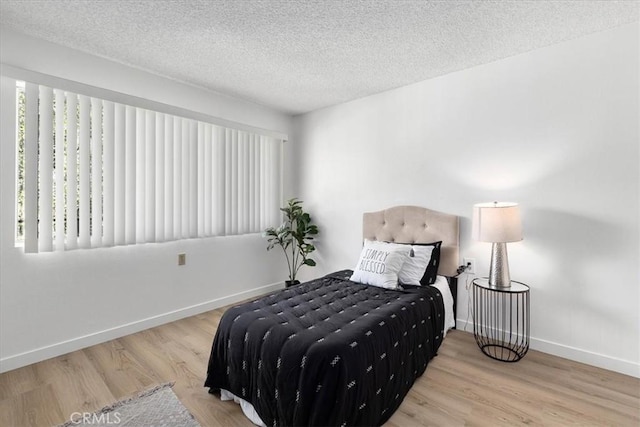 bedroom with baseboards, a textured ceiling, and wood finished floors