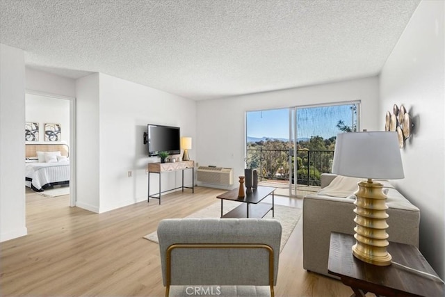 living room featuring a textured ceiling, a wall mounted AC, baseboards, and wood finished floors