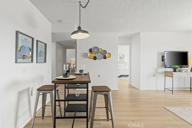 dining space featuring a textured ceiling, light wood-type flooring, and baseboards