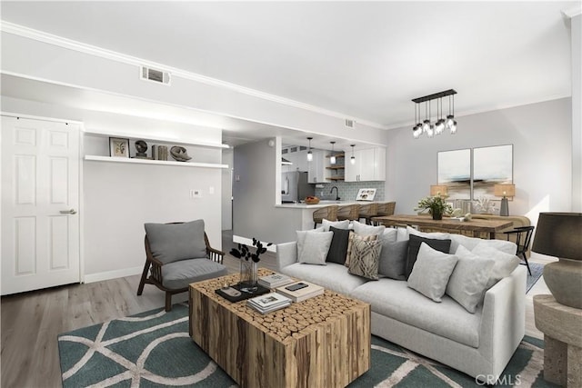 living room with visible vents, a notable chandelier, light wood-style flooring, crown molding, and baseboards