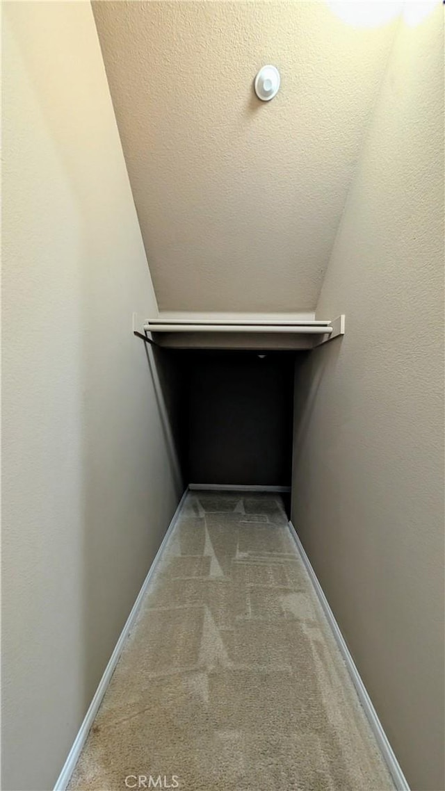 hall featuring baseboards, a textured ceiling, and light colored carpet