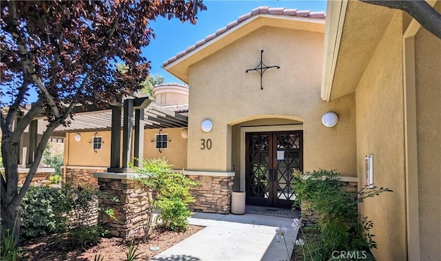 view of exterior entry featuring stone siding, a tile roof, french doors, and stucco siding