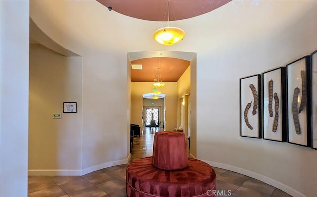 hallway featuring arched walkways, tile patterned flooring, and baseboards