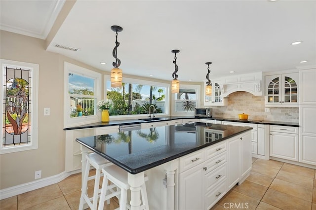 kitchen with a sink, glass insert cabinets, a kitchen island, light tile patterned floors, and decorative backsplash