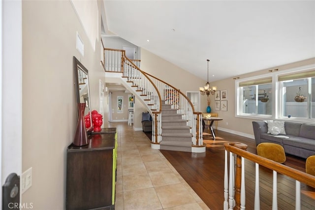 foyer entrance with wood finished floors, baseboards, high vaulted ceiling, an inviting chandelier, and stairs