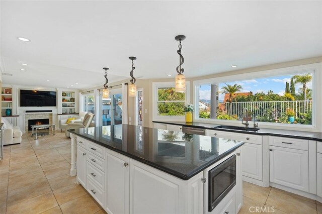 kitchen with a kitchen island, light tile patterned floors, a warm lit fireplace, appliances with stainless steel finishes, and a sink