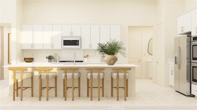 kitchen featuring white cabinets, stainless steel appliances, light countertops, a kitchen bar, and a sink