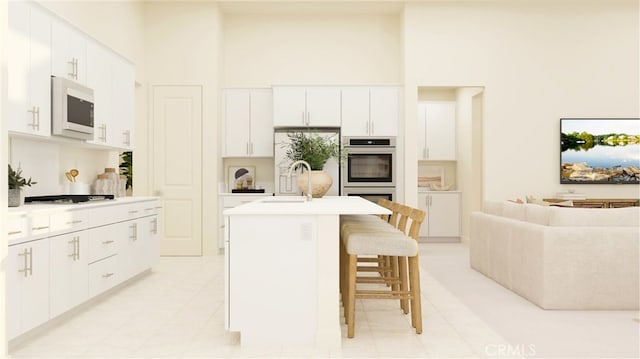 kitchen with a towering ceiling, white microwave, a breakfast bar, a kitchen island with sink, and a sink