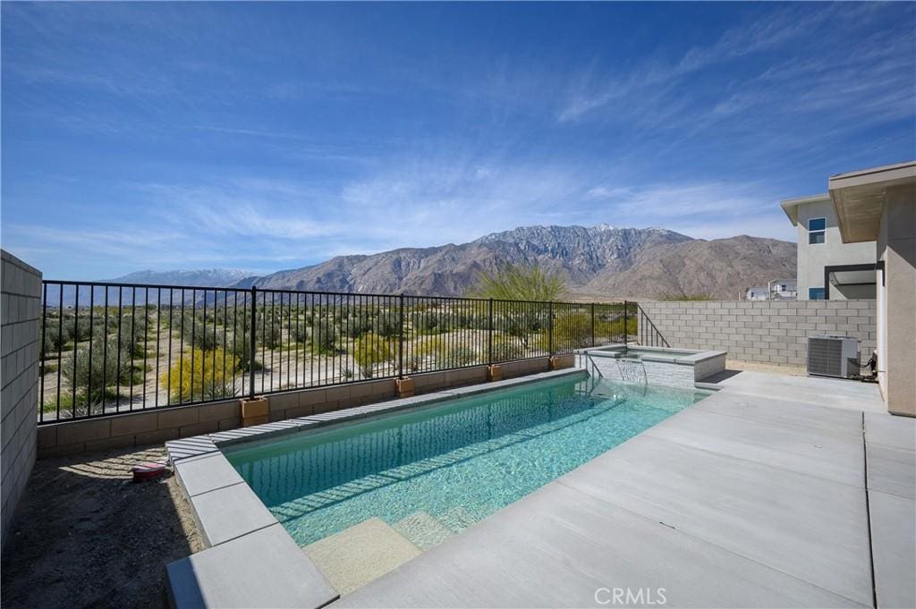 view of pool with a pool with connected hot tub, fence, cooling unit, a patio area, and a mountain view