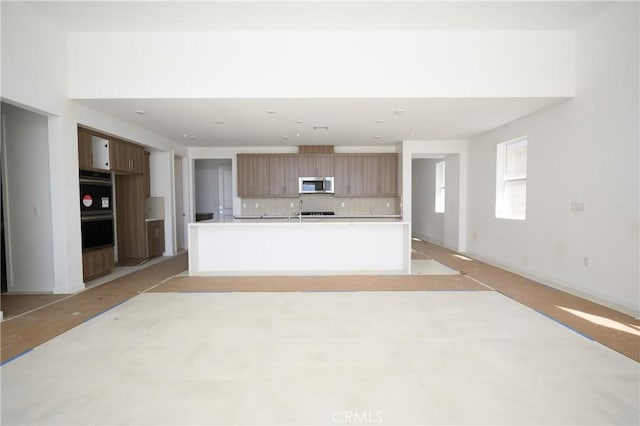 kitchen featuring stainless steel microwave, light countertops, decorative backsplash, modern cabinets, and dobule oven black