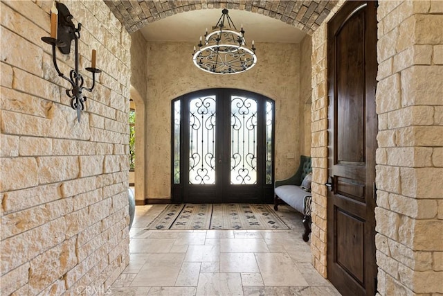 entryway with arched walkways, french doors, stone tile flooring, an inviting chandelier, and brick ceiling