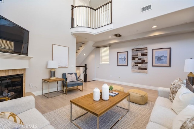 living area featuring baseboards, visible vents, a tiled fireplace, and wood finished floors