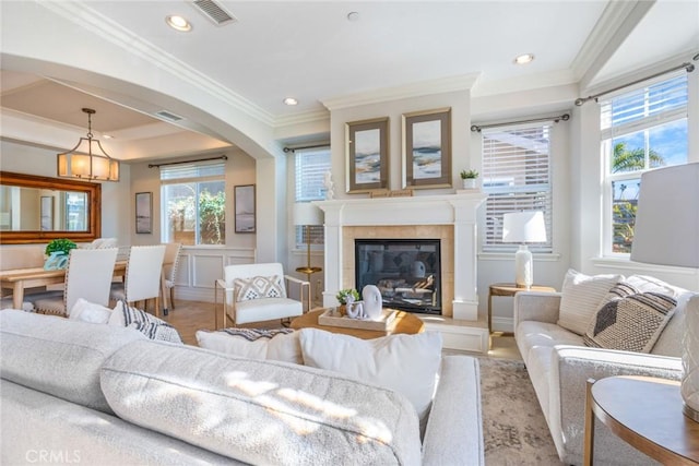 living area with ornamental molding, arched walkways, visible vents, and a fireplace