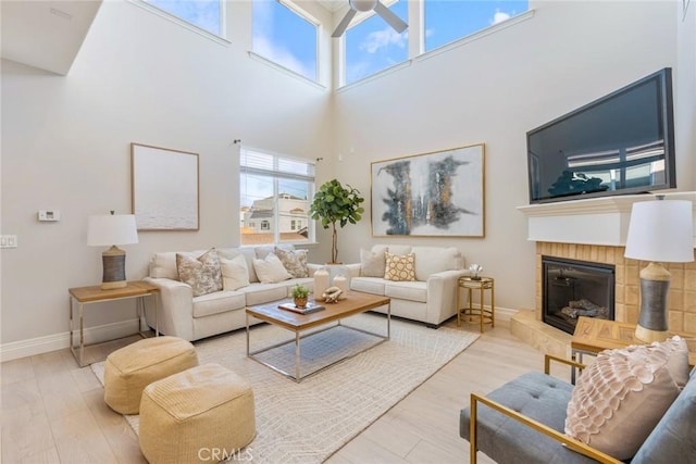 living room with wood finished floors, a tile fireplace, a towering ceiling, and baseboards