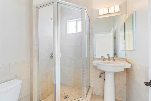 bathroom featuring toilet, a stall shower, tile walls, and a wainscoted wall