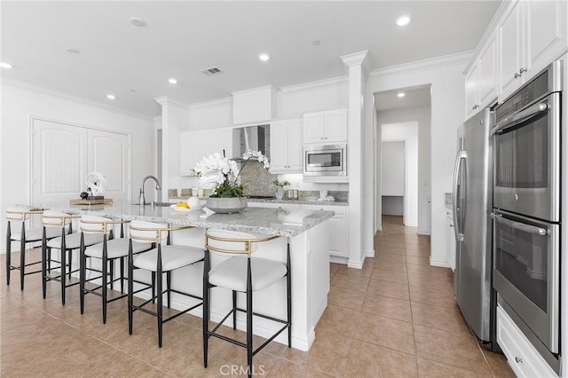 kitchen featuring wall chimney range hood, ornamental molding, light tile patterned floors, appliances with stainless steel finishes, and white cabinetry