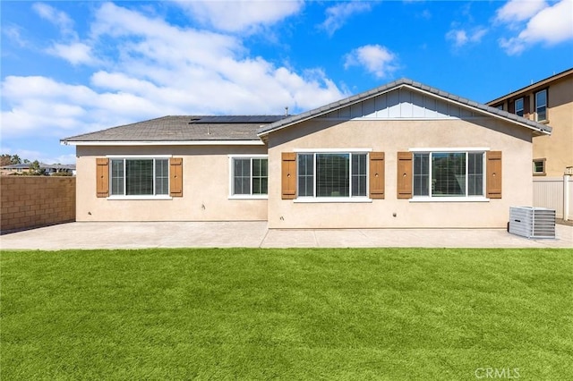 back of house with a patio, a lawn, roof mounted solar panels, and fence