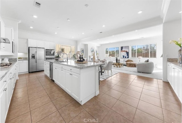 kitchen featuring visible vents, a sink, appliances with stainless steel finishes, crown molding, and open floor plan