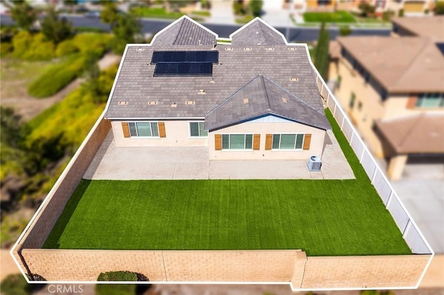 back of house featuring a fenced backyard, roof mounted solar panels, a lawn, and a patio