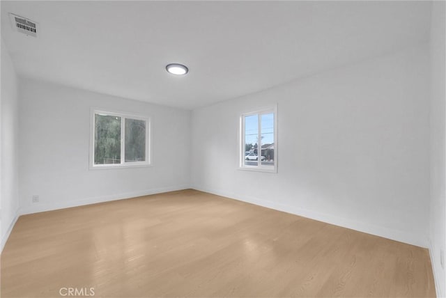 empty room featuring wood finished floors, visible vents, and baseboards